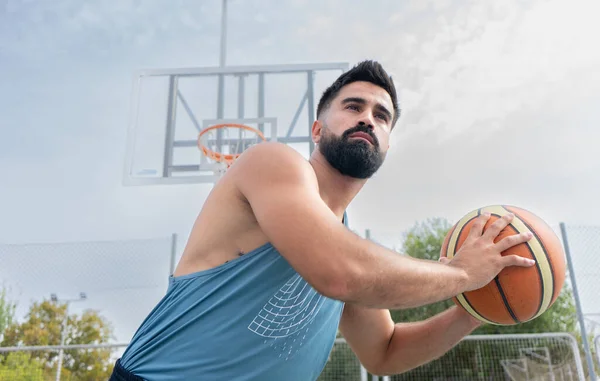 Mavi tişörtlü çocuk güneşli bir günde dışarıda basketbol oynuyor.
