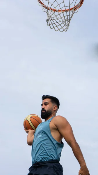 Mavi tişörtlü çocuk güneşli bir günde dışarıda basketbol oynuyor.