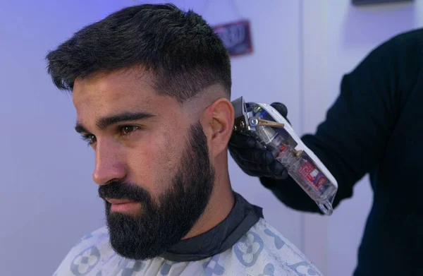 Berber kuaförde beyaz bir adamın saçını kesiyor. Berberin bir saç makası var. Ayrıntılı çekimleri olan yatay bir resim..