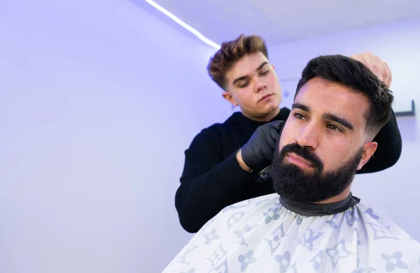 Berber kuaförde beyaz bir adamın saçını kesiyor. Berberin bir saç makası var. Ayrıntılı çekimleri olan yatay bir resim..