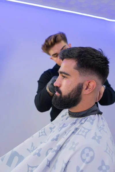 Berber kuaförde beyaz bir adamın saçını kesiyor. Berberin bir saç makası var. Ayrıntılı çekimleri olan yatay bir resim..