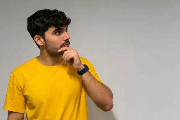 Beyaz, beyaz, kıvırcık saçlı, sarı tişörtlü, tenha beyaz arka planda düşünceli beyaz çocuk.