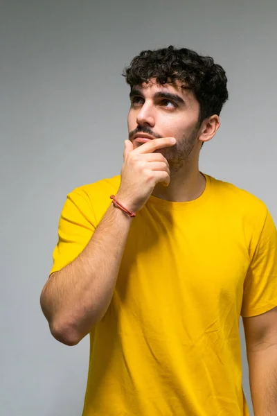 Beyaz, beyaz, kıvırcık saçlı, sarı tişörtlü, tenha beyaz arka planda düşünceli beyaz çocuk.