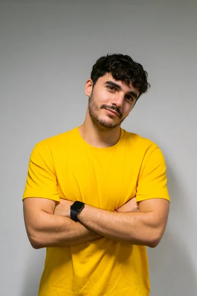 Beyaz, beyaz, kıvırcık saçlı, sarı tişörtlü, kolları çapraz beyaz tenli.