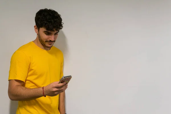 Beyaz, beyaz, kıvırcık saçlı ve sarı tişörtlü bir çocuk izole edilmiş beyaz arka plan üzerinden cep telefonuna bakıyor.