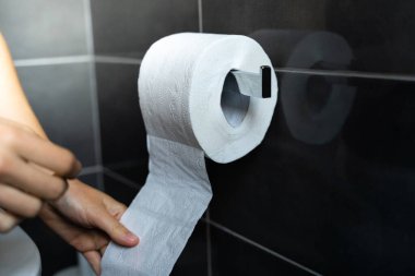 Banyodaki metal tutacaktan sarkan bir rulo tuvalet kağıdı alan eli kapat. İshal kavramı, mide ağrısı. Sağlık sigortası konsepti. Tuvalette oturan kadın.. 