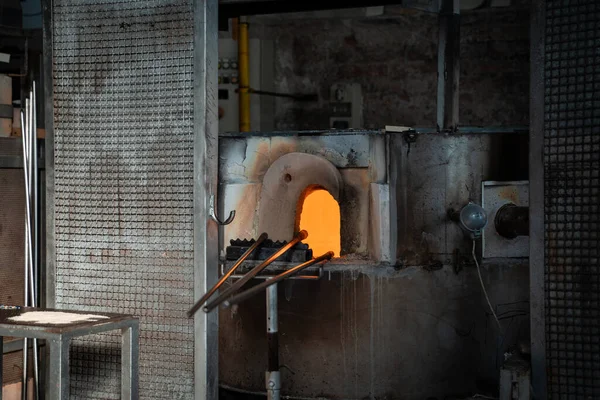 stock image Murano glass blowing factory. Workers put iron rod in furnace to make glass malleable.Artist shaping hot glass into a figurine with gas flames. Artisan making glass vases and sculptures. Venice winter. Glass melting in a traditional oven.