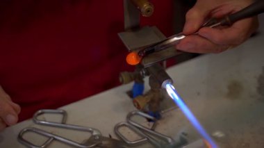 Murano glass blowing factory. Workers put iron rod in furnace to make glass malleable.Artist shaping hot glass into a figurine with gas flames. Artisan making glass vases and sculptures. Venice winter. Glass melting in a traditional oven of a glass