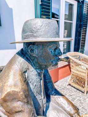 Şapkalı, mavi gömlekli, sakallı ve siyah ceketli bir adamın heykeli eski şehrin sokaklarında. 