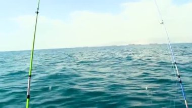 Uçsuz bucaksız, sakin okyanusa bakan bir teknede bulunan sakin bir olta sahnesi. Arka plan, açık gökyüzünün altında uzak bir gemi hattını ve puslu bir kıyı şeridini gözler önüne seriyor. Denizde balık tutarak geçirilen bir günün huzurlu ve geniş hissini yakalıyor..