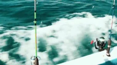 Teknenin yan tarafında sallanan kancalı bir olta ve arka planda kayığın hareketleriyle okyanus suyu bulanıklaşıyor. Hareket halindeki bir balık avının dinamik enerjisini yakalar. Balık tutmanın heyecanıyla denizin güzelliğini birleştirir..