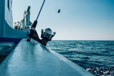 Bir balıkçı oltası ve makarası açık mavi denizde ilerlerken bir teknenin kenarına kurulur ve açık bir gökyüzünün altında balık avı için mükemmel bir sahne yaratır.