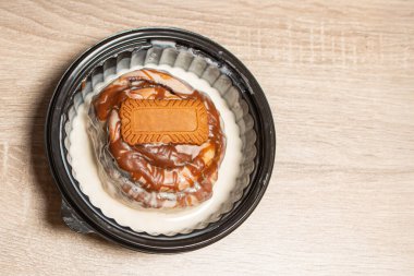 Karamel soslu tek bir lezzetli tarçınlı çörek ve siyah bir kasede spekülasyon bisküvisi fotokopi alanı olan açık ahşap bir masada.