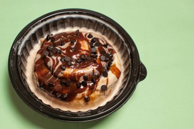 Beyaz kremalı çikolata sosuyla kaplı bir tarçınlı tarçınlı börek ve siyah plastikle servis edilen mini çikolatalı cips.