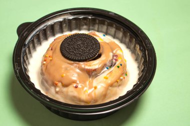 Beyaz şekerle kaplı tarçınlı börek ve üzeri çikolatalı sandviç kurabiyesi ve yeşil bir masada duran siyah bir kasenin içine serpiştirilmiş krema.