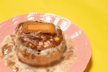 Eriyen kremalı kremayla ıslanmış taze tarçınlı çörek ve üzerinde sarı arka planı olan spekülasyonlu bisküvi ile zengin karamel sosu.