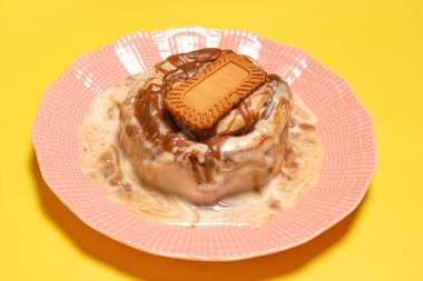 Eriyen kremalı kremayla ıslanmış taze tarçınlı çörek ve üzerinde sarı bir arka planda pembe bir tabakta spekulolu bisküvi olan zengin karamel sosu.