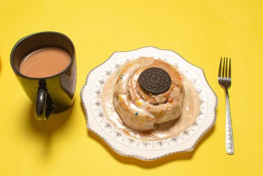 Nefis bir tarçınlı tarçınlı çörek çikolatalı sandviç ve çatallı bir tabak ve parlak sarı bir arka planda bir kupa kahve.
