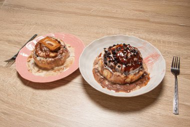 İki çeşit tarçınlı dürüm, biri çikolatalı, diğeri de karamelli bisküvili ve ahşap bir arka planda çatalla servis edilmiş.