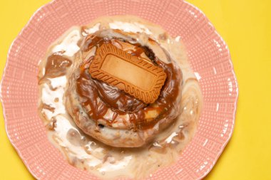 Karamel soslu tatlı tarçınlı çörek ve parlak sarı bir zemin üzerinde dokulu pembe bir tabakta servis edilen spekülasyonlu bisküvi.