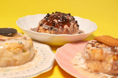 Üç gurme tarçınlı çöreğin bir karışımı. Tabaklarda farklı malzemeler var. Parlak sarı arka planda seçici bir odak noktası çikolata parçacıklı pasta.