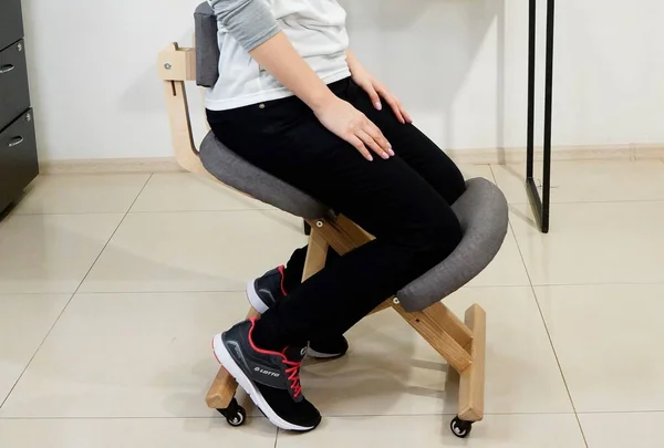 Woman is Sitting on Therapeutic Kneeling Chair in Office. Ergonomic Chair Using. Modern Office Stool for Spine Health and Wellness. Furniture for Remote Work and Study.
