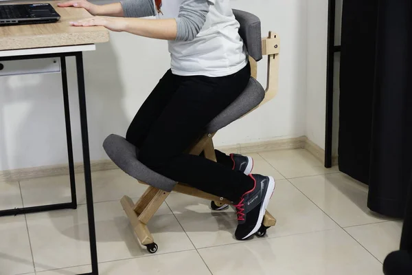 Female Freelancer is Sitting on Kneeling Chair at Home Office. Ergonomic Chair Using. Modern Office Stool for Spine Health and Wellness. Furniture for Remote Work and Study.