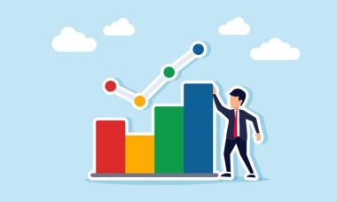 İş adamı bir grafiğin, iş ilerlemesinin ve ürün satışlarının resimlerinin yanında duruyor