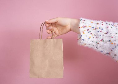 Beyaz örgü bluzlu bir kız. Elinde pembe pastel arka planda bir kesekağıdı var.