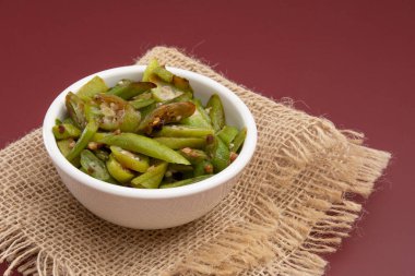 Grilled okra, in a white bowl on a red background, focused, isolated