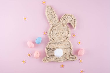Handmade easter bunny made of strings with eggs and flowers on a light pink background