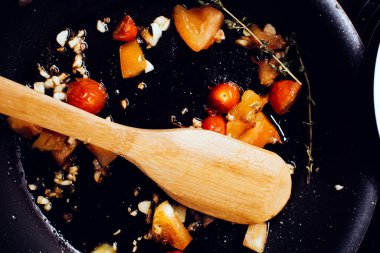 Frying tomatoes and herbs on a pan, top view, wooden spoon