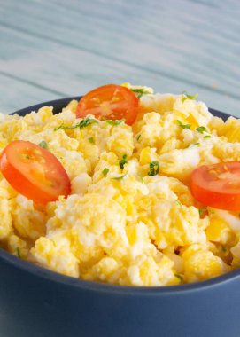 Scrambled eggs on bowl, wooden table, vertical