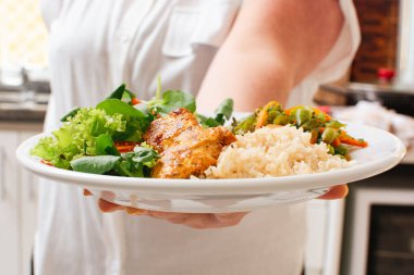 Kadın tarafından servis edilen ızgara tavuk, pilav, salata ve sebzeli sağlıklı yemek.