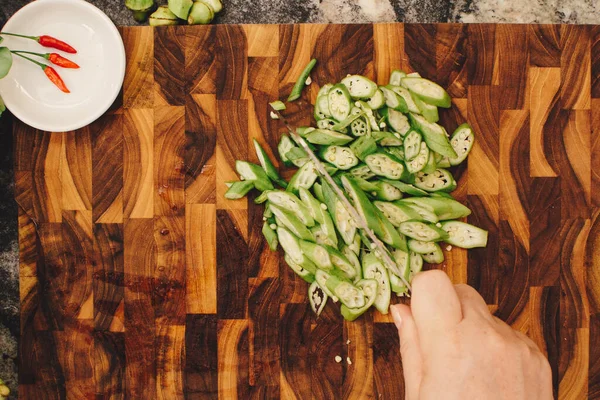 Stock image Top-down photo of female hand cutting okra on wooden cutting board for cooking