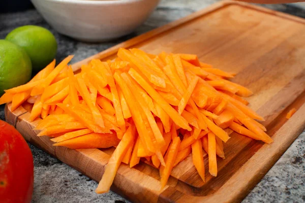 Close-up photo of carrots cut into strips on a wooden cutting board
