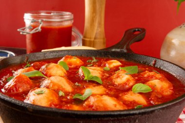 Kırmızı domates soslu lezzetli Gnocchi ve Fesleğen siyah tavada servis ediliyor. Kırmızı arka planda.