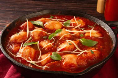 Lezzetli Gnocchi, kırmızı domates soslu ve fesleğenli, siyah tavada servis edilen ahşap arka planda.