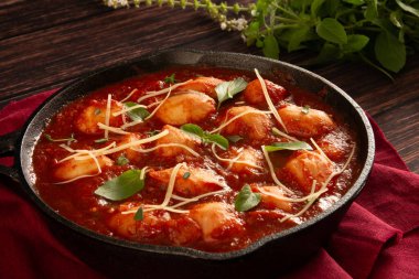 Lezzetli Gnocchi, kırmızı domates soslu ve fesleğenli, siyah tavada servis edilen ahşap arka planda.