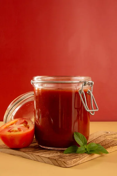 在玻璃瓶里放上新鲜的番茄酱和罗勒叶 前面是一片红色背景的西红柿 — 图库照片