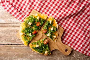 Arugula, ahşap bir masanın üzerinde kırmızı bir piknik beziyle servis edilen ahşap bir kesme tahtasıyla servis edilen el yapımı pizza.