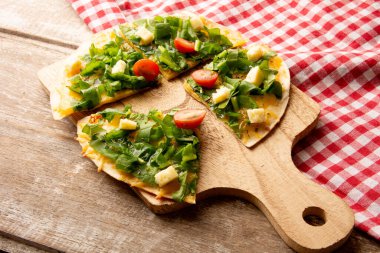 Arugula, ahşap bir masanın üzerinde kırmızı bir piknik beziyle servis edilen ahşap bir kesme tahtasıyla servis edilen el yapımı pizza.