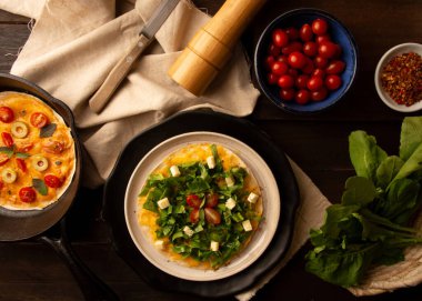 Arugula pizza tavası içinde peynir ve kiraz domatesli el yapımı seramik tabak içinde ahşap bir masanın üstünde, Arugula pizza tavasında peynirli ve vişneli domatesli ahşap bir masanın üstünde.