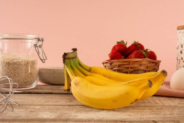 Muz ve çilek bambu sepetinin içinde, ahşap bir masanın üstünde pembe bir arka planda.