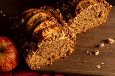 Lezzetli Elmalı Yulaf ekmeği, karanlık ve kasvetli stüdyo ışıklarıyla ahşap bir kesim tahtasında.