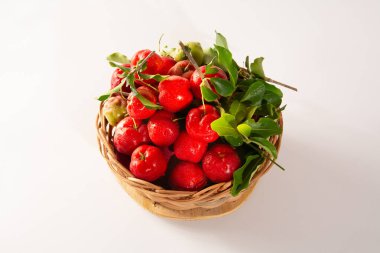 Taze toplanmış organik Acerolas bir sepetin içinde beyaz bir masanın üzerinde ve temiz bir arkaplan önde.