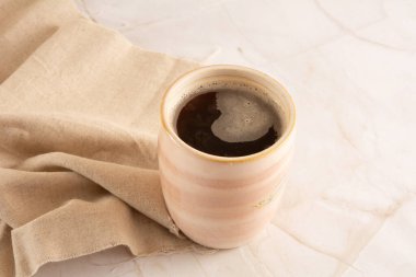 Önünde bej peçete olan mermer bir arka planda kahve fincanı.