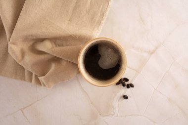 Mermer bir arka planda kahve fincanı, bej peçete ve kahve çekirdekleri havadan görünüşlü.