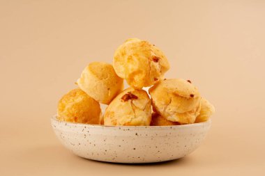 Brezilya peynirli ekmek, seramik bir kasenin içine izole edilmiş, öndeki temiz bej arka planda.