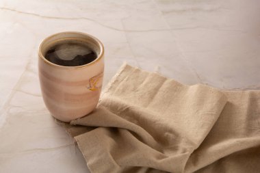Önünde bej peçete olan mermer bir arka planda kahve fincanı.